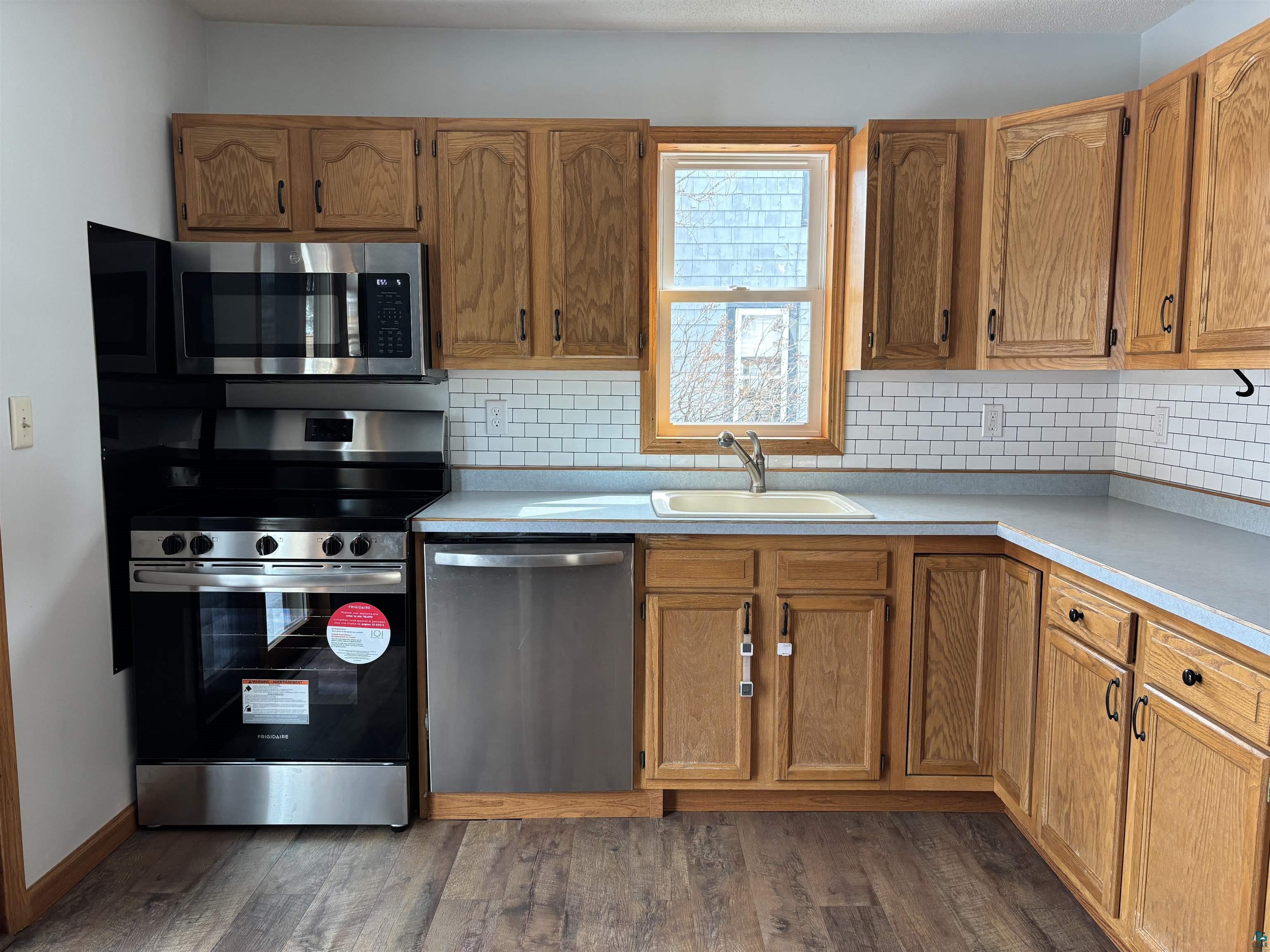 21 4th Street Proctor, MN 55810 - Photo 19 of 35 Kitchen featuring light countertops, dark wood-type flooring, decorative backsplash, a sink, and appliances with stainless steel finishes
