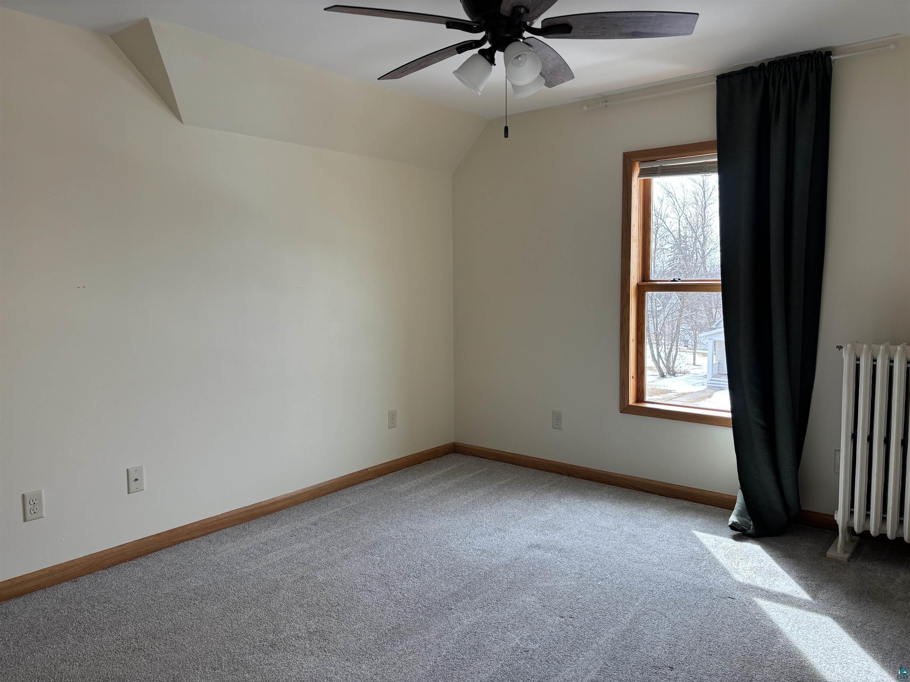 21 4th Street Proctor, MN 55810 - Photo 25 of 35 Empty room with vaulted ceiling, radiator heating unit, baseboards, light colored carpet, and ceiling fan