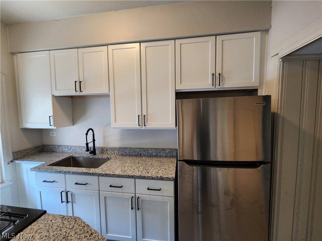 7202 Snow Road Parma, OH 44129 - Photo 4 of 14 Kitchen with white cabinetry, stainless steel refrigerator, black stovetop, light stone counters, and sink