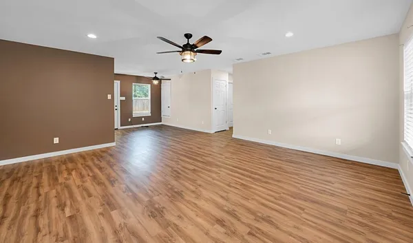 an empty room with wooden floor ceiling fan and windows
