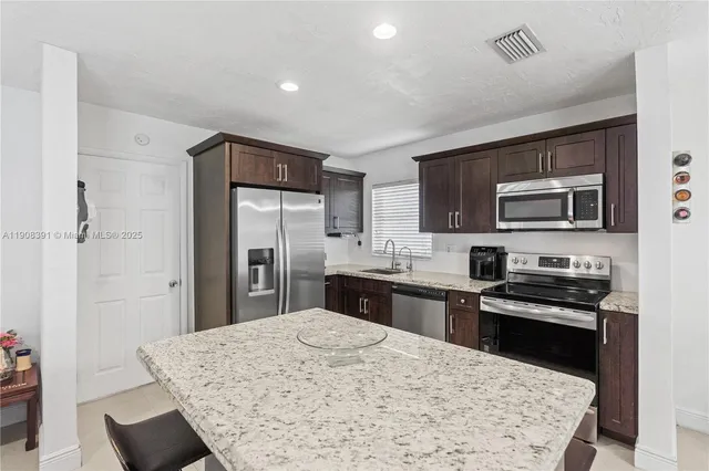 a kitchen with stainless steel appliances kitchen island granite countertop a refrigerator and a stove top oven