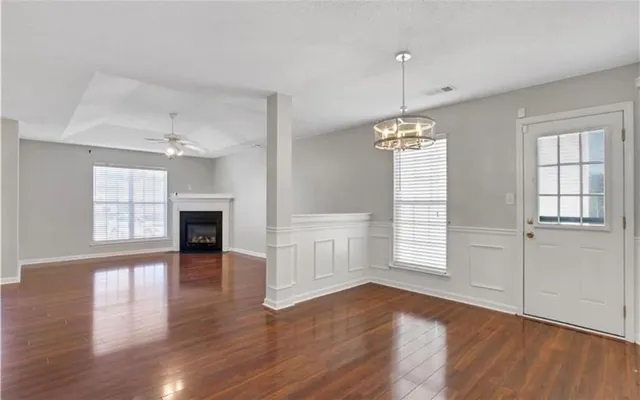 an empty room with wooden floor chandelier and windows