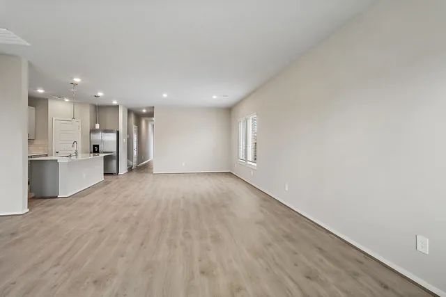 a view of an empty room with wooden floor kitchen view and a window