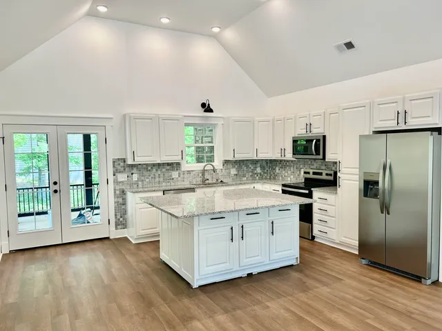 a large kitchen with stainless steel appliances a large counter top a stove a refrigerator cabinets and a wooden floor