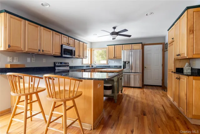 a kitchen with stainless steel appliances granite countertop wooden cabinets a refrigerator a stove a sink and a microwave with wooden floor