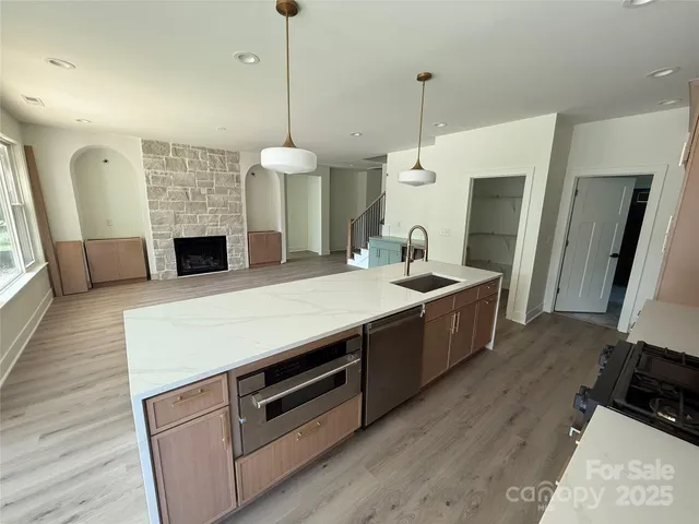 a living room with stainless steel appliances kitchen island granite countertop a stove a sink a refrigerator a couch and a fireplace with wooden floor