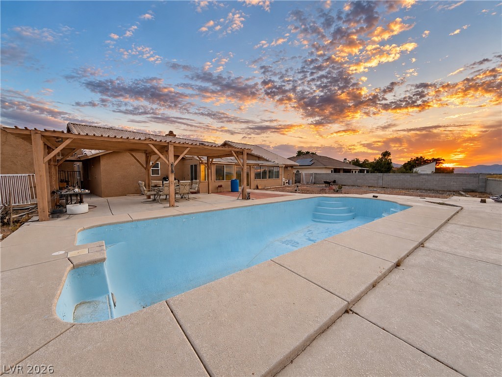 5470 Grain Mill Road Pahrump, NV 89061 - Photo 53 of 80 16x40 pool is 8.5' deep with cool decking surrounding it. An expansive concrete patio surrounds the in-ground pool under a rustic wooden pergola structure.
