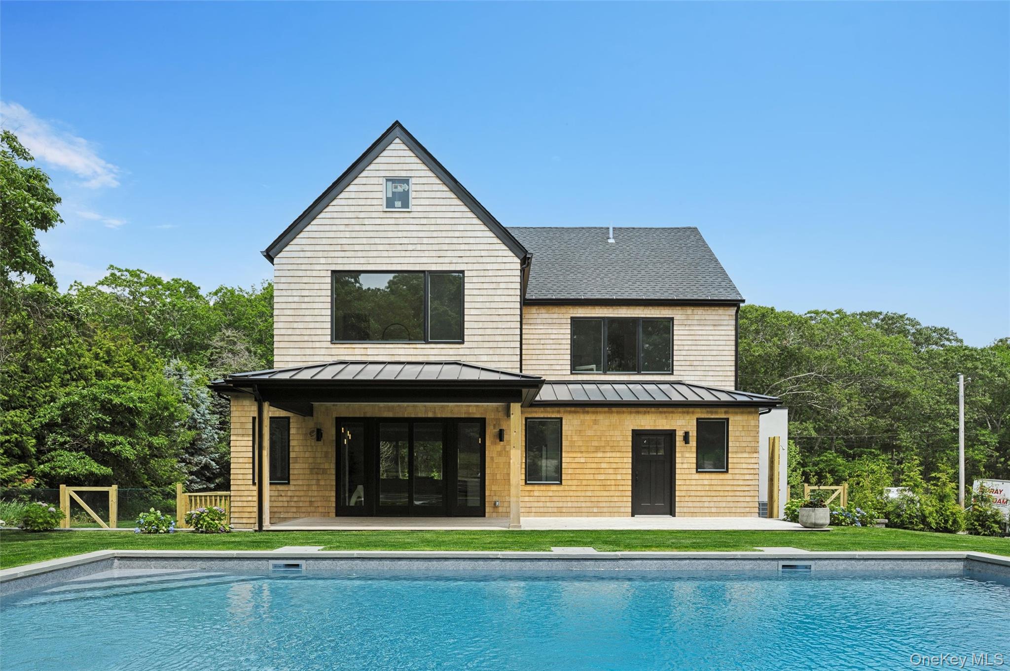 Rear view of house featuring a standing seam roof, an outdoor pool, a patio, a shingled roof, and metal roof