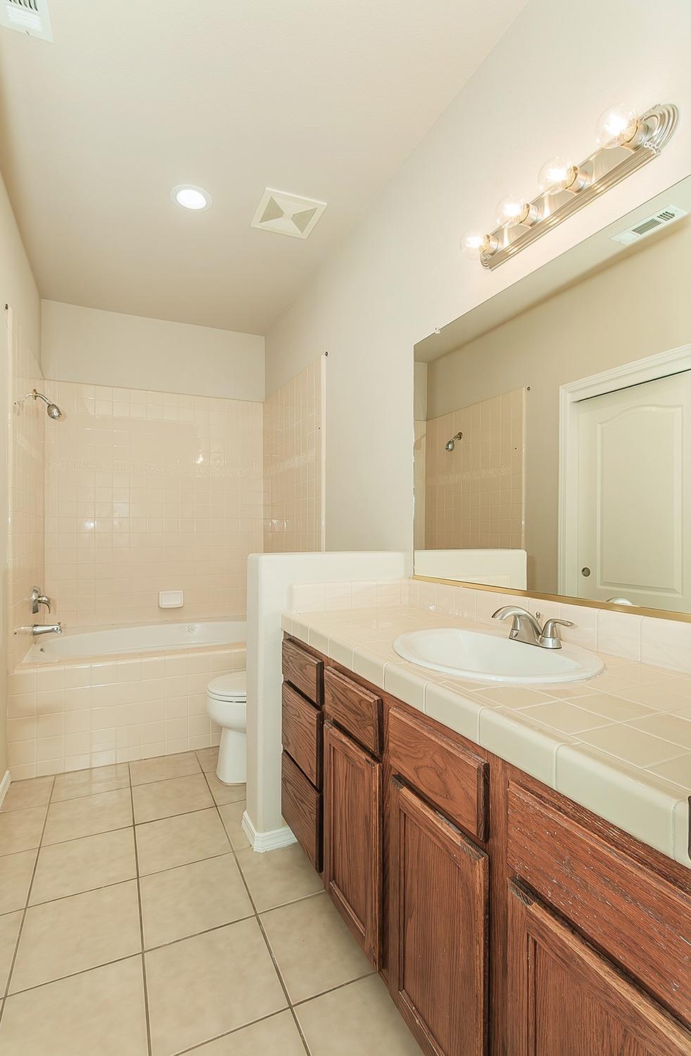 735 West Brittany Lane Clovis, CA 93619 - Photo 16 of 30 a bathroom with a granite countertop sink a toilet a mirror and bathtub