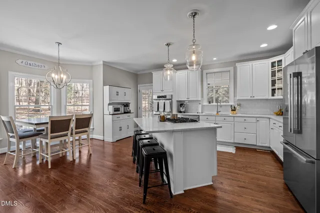 a kitchen with stainless steel appliances a dining table chairs stove refrigerator and cabinets