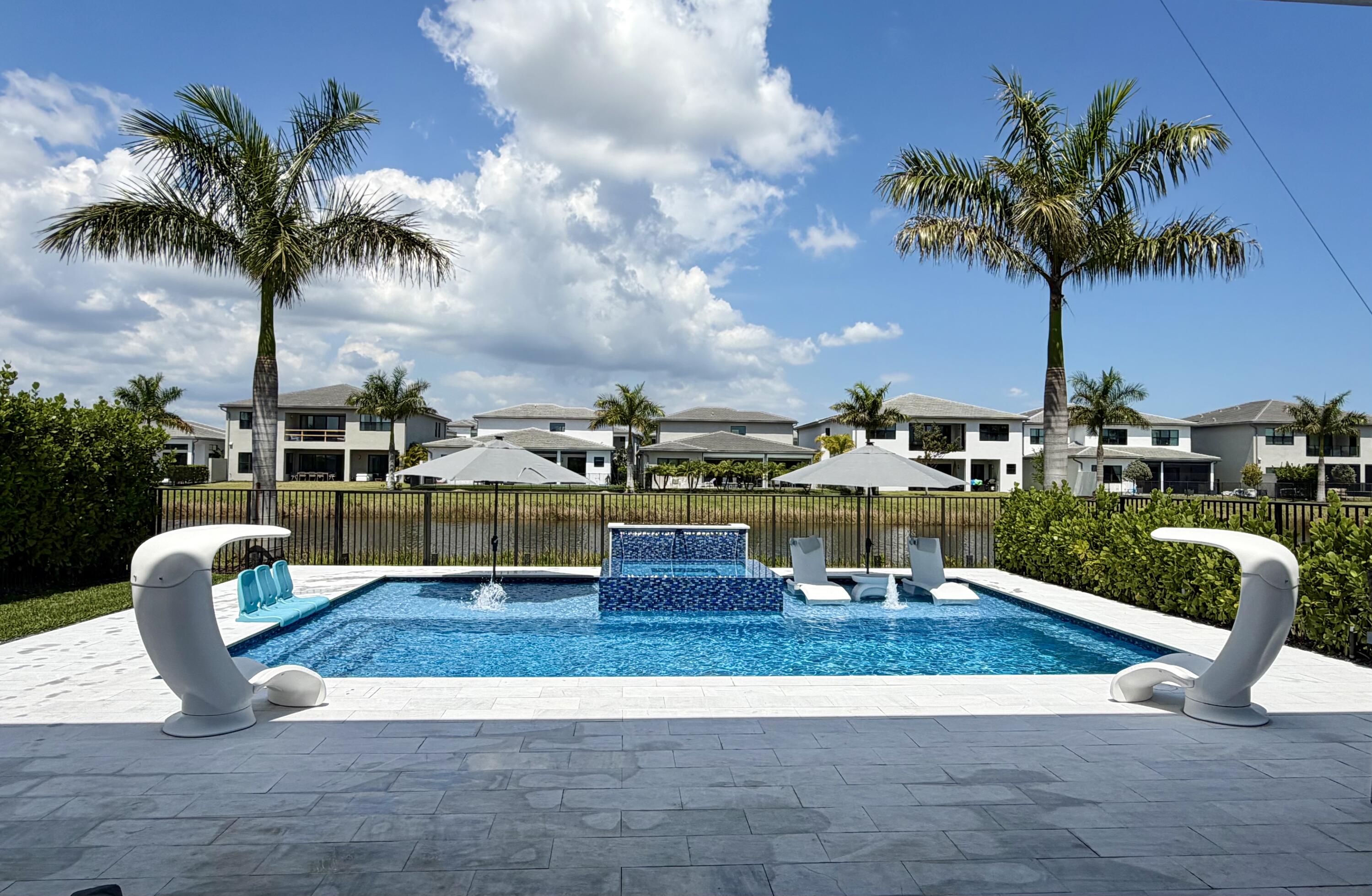 8573 Crystal Downs Avenue Boca Raton, FL 33434 - Photo 53 of 82 a view of a swimming pool with a lawn chairs under palm trees