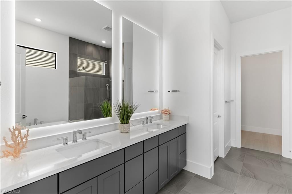 19084 Gentry Place Estero, FL 33928 - Photo 23 of 44 Primary bath with dual sinks, backlit mirrors, gray cabinetry, and Calacatta countertops