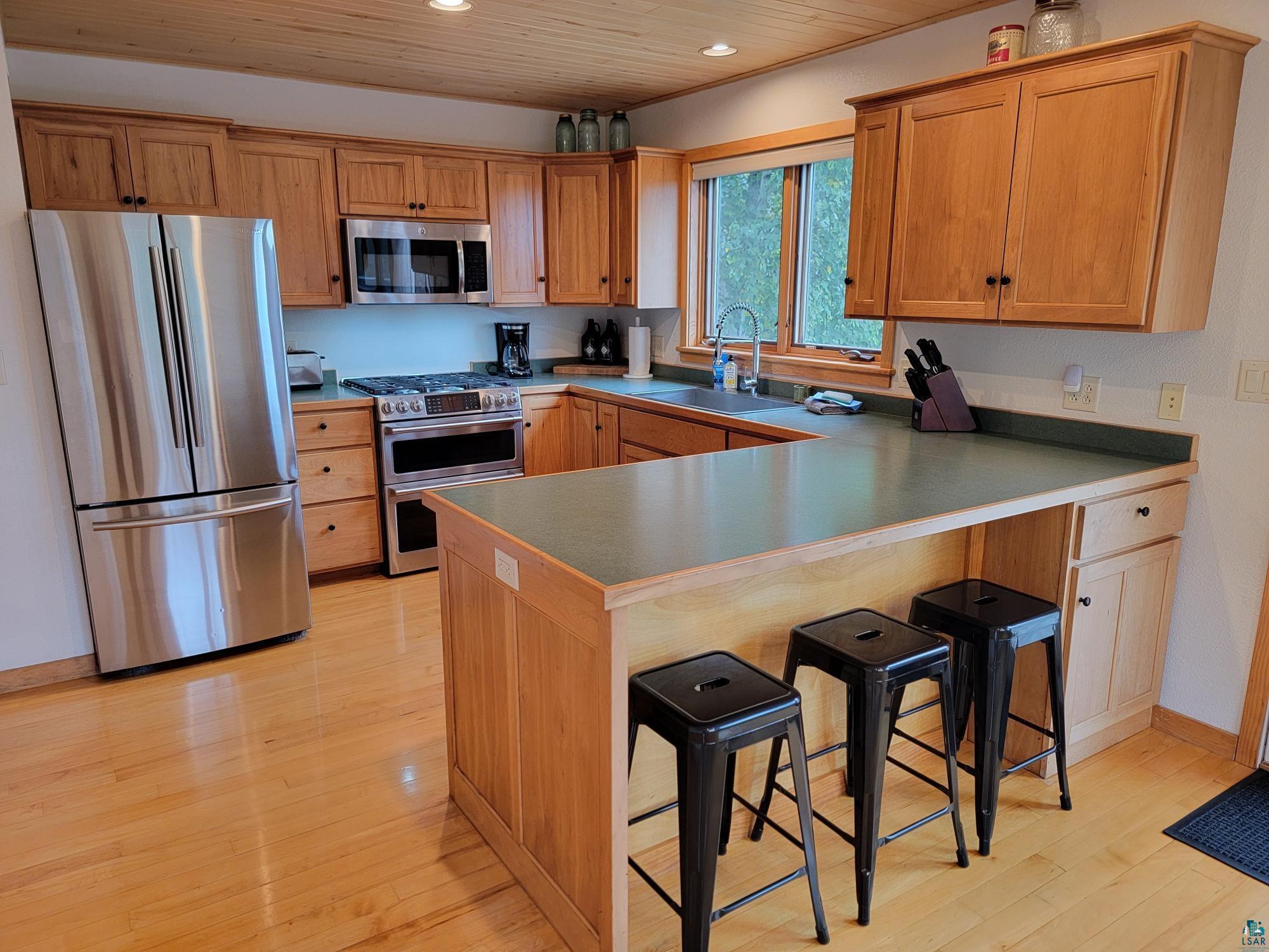 184 Fall River Road Grand Marais, MN 55604 - Photo 24 of 50 Kitchen featuring light wood-type flooring, stainless steel appliances, kitchen peninsula, sink, and a breakfast bar