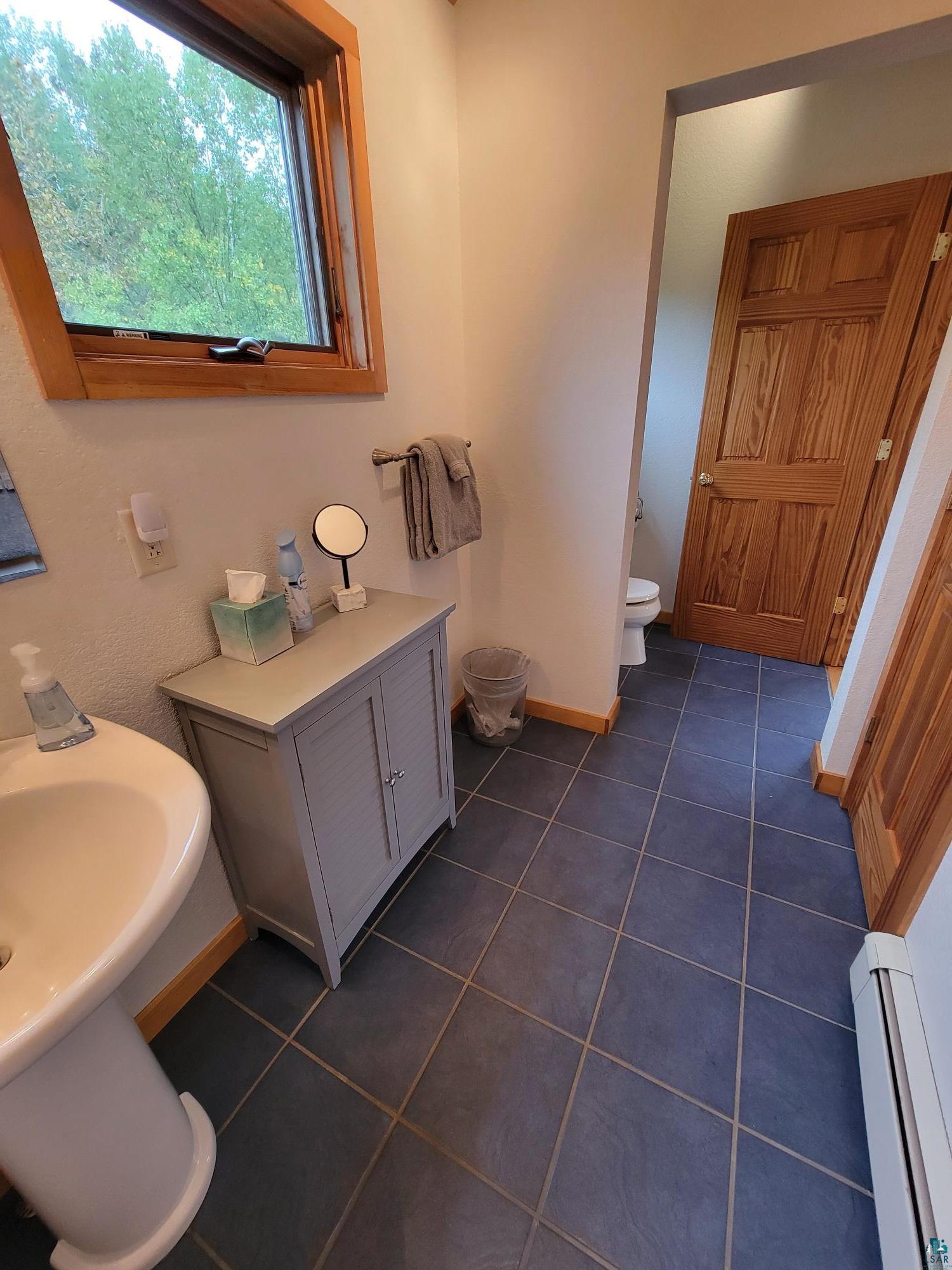 184 Fall River Road Grand Marais, MN 55604 - Photo 32 of 50 Bathroom with toilet, sink, a baseboard radiator, and tile patterned floors