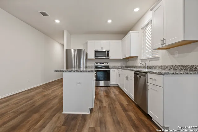 a kitchen with granite countertop wooden floors stainless steel appliances and white cabinets