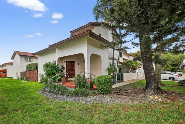 a view of a white house with potted plants and a large tree