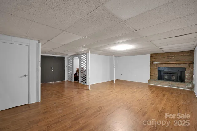 a view of an empty room with wooden floor fireplace and a window