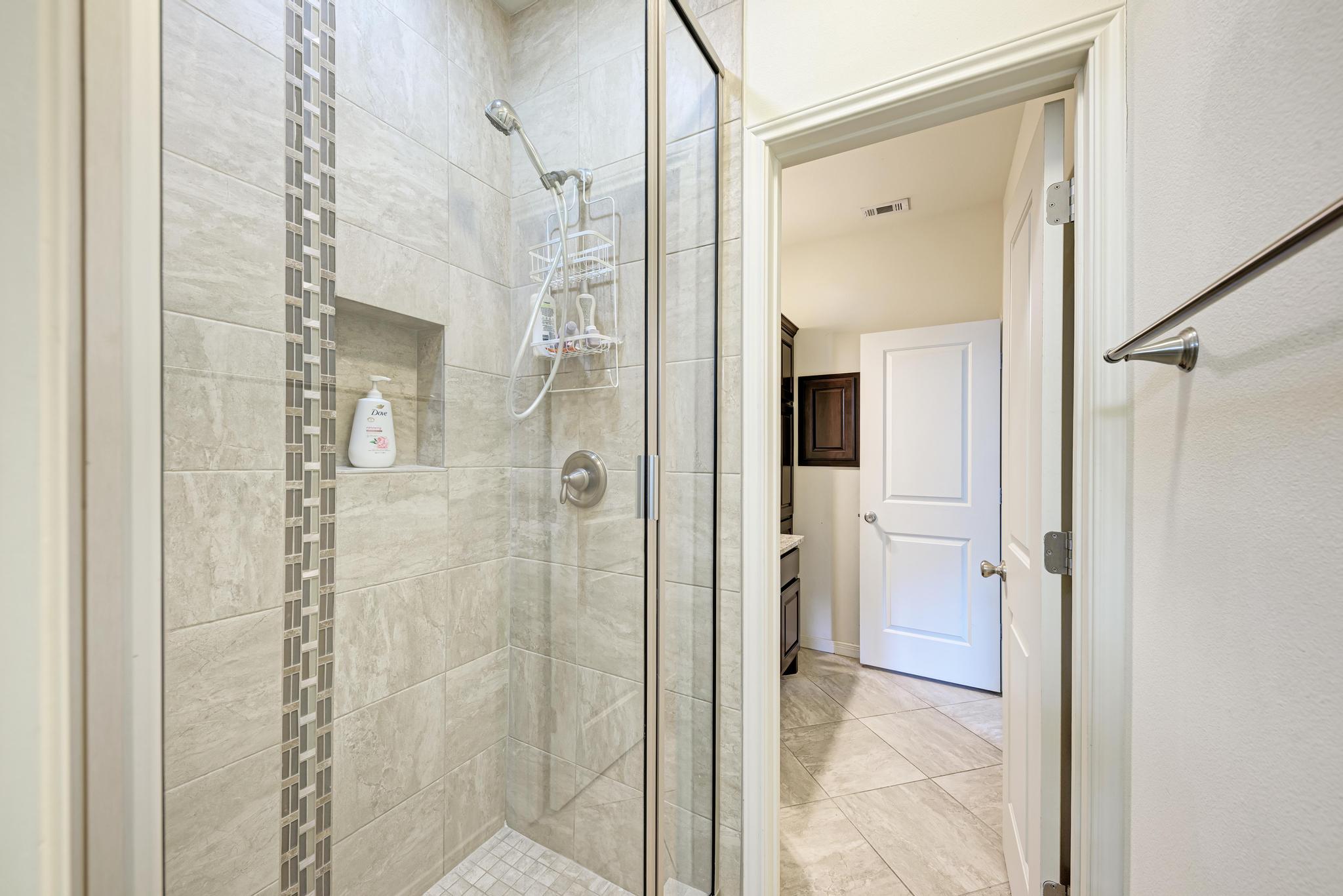 2605 Indian Creek Road Austin, TX 78734 - Photo 21 of 33 Glass-enclosed shower with light-toned tiled walls, a decorative vertical tile accent, a recessed niche, and a brushed nickel showerhead