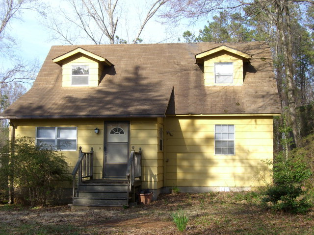 a view of a brick house with large windows and a yard with plants and large trees