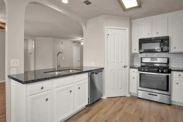a kitchen with stainless steel appliances granite countertop a sink a stove a refrigerator and white cabinets