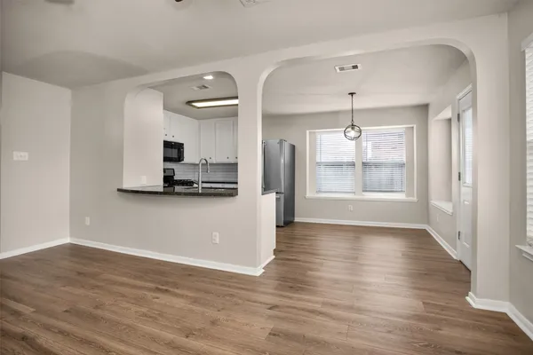 a view of an empty room with kitchen and window
