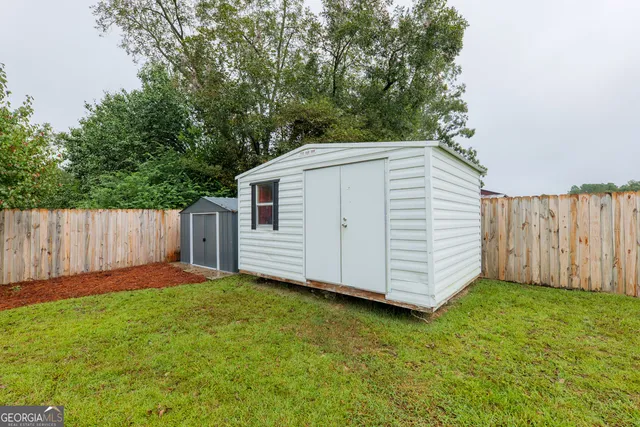 a view of a backyard with white wall and wooden fence