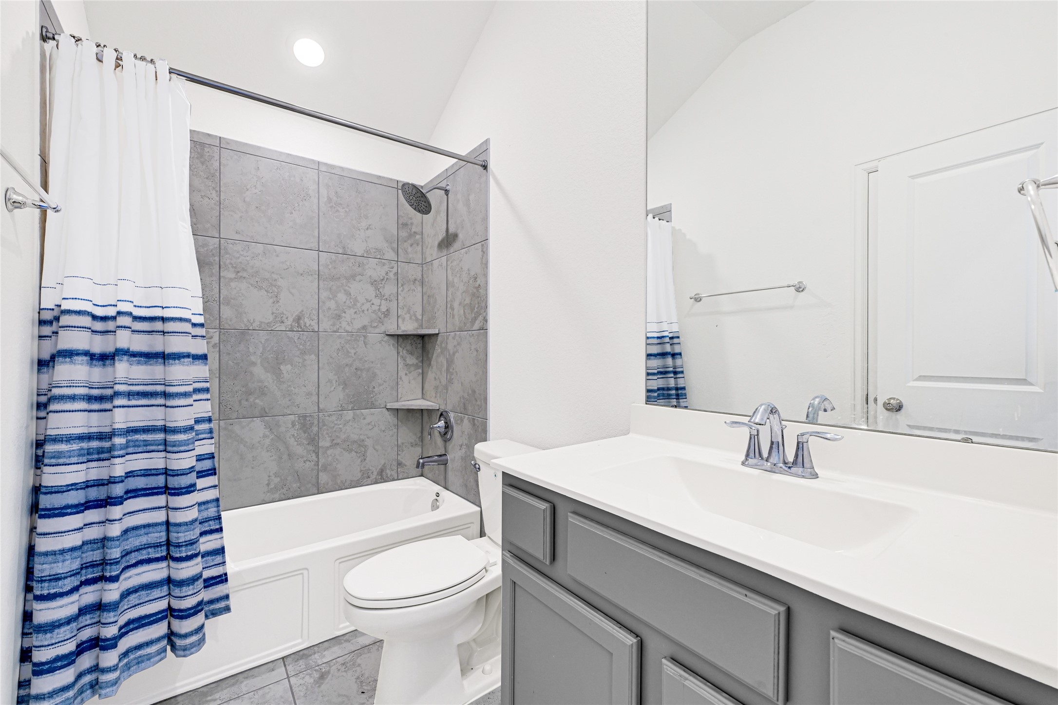 4307 Annandale Lane Rosharon, TX 77583 - Photo 19 of 31 This modern bathroom features a sleek vanity with a large mirror, a bathtub with a grey tiled shower, and a stylish blue and white striped shower curtain. The space is bright and clean, with contemporary fixtures and ample lighting.