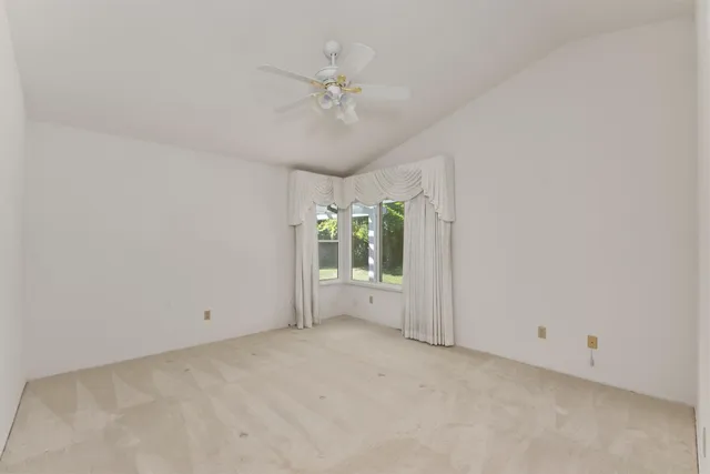 an empty room with chandelier fan and windows