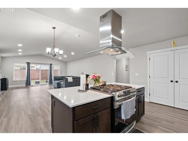 a kitchen with a stove a kitchen island a sink dishwasher a dining table and chairs with wooden floor