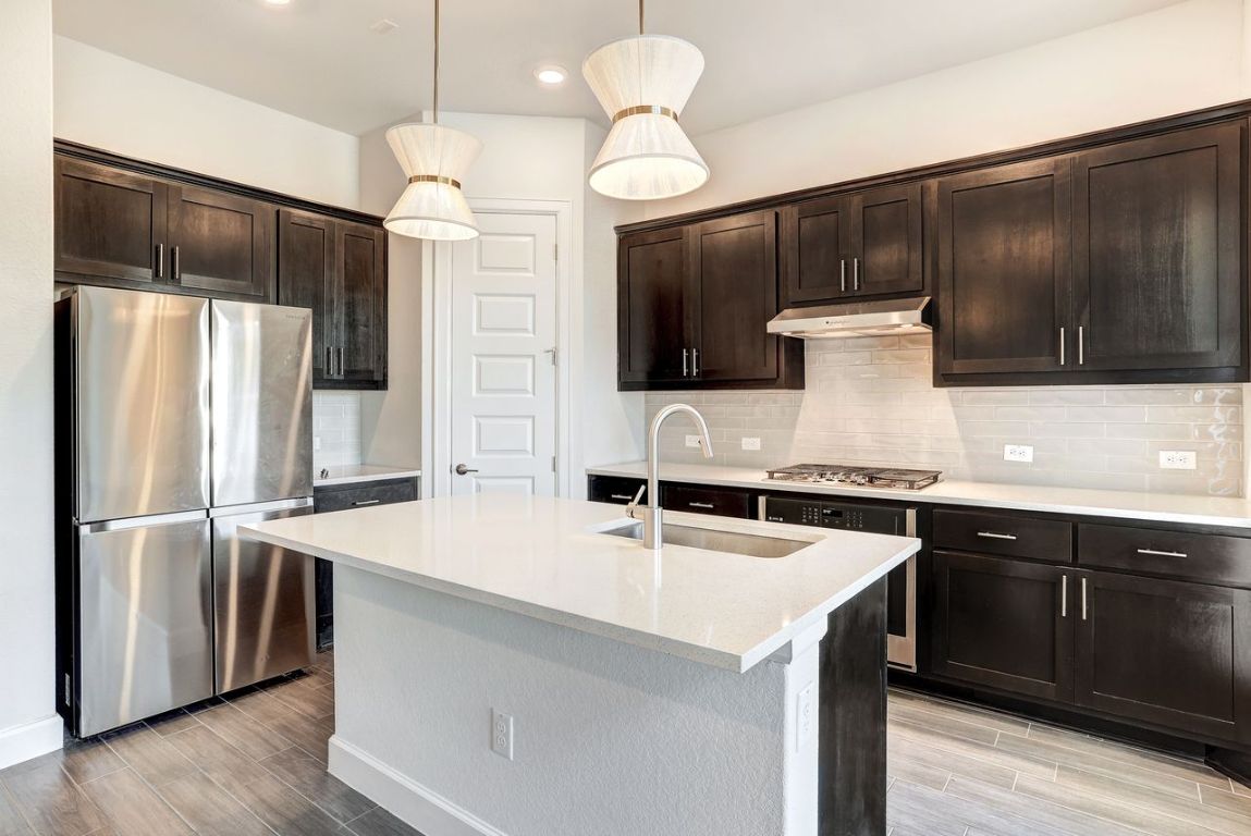 4705 Sea Salt Drive Austin, TX 78747 - Photo 6 of 19 Kitchen with stainless steel appliances, dark brown cabinetry, light stone counters, and wood finish floors