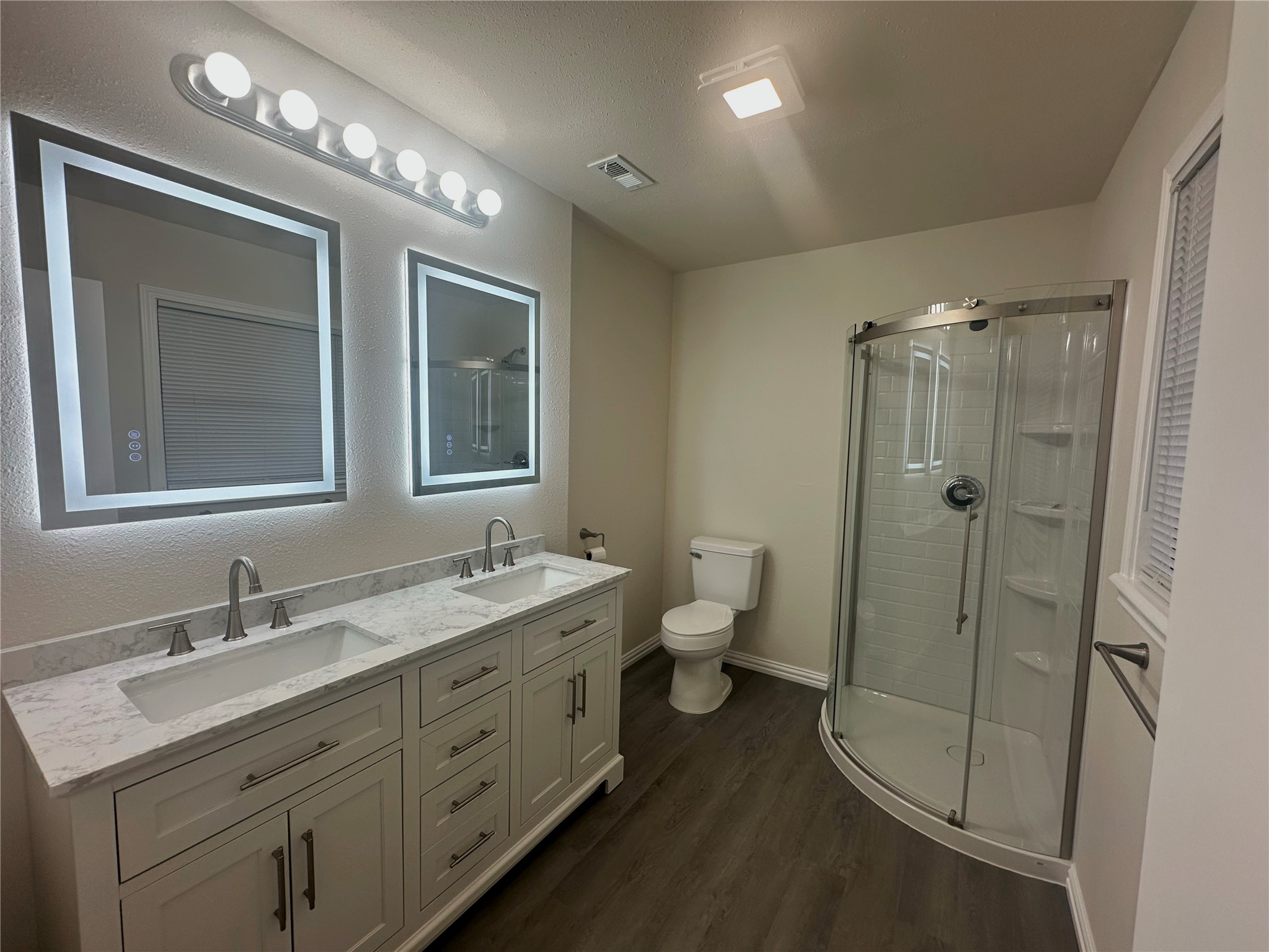 130 Bay Ridge Drive Baytown, TX 77523 - Photo 14 of 20 Modern bathroom featuring a double vanity with illuminated mirrors, a sleek corner shower with glass doors, and wood-look flooring for a contemporary feel.