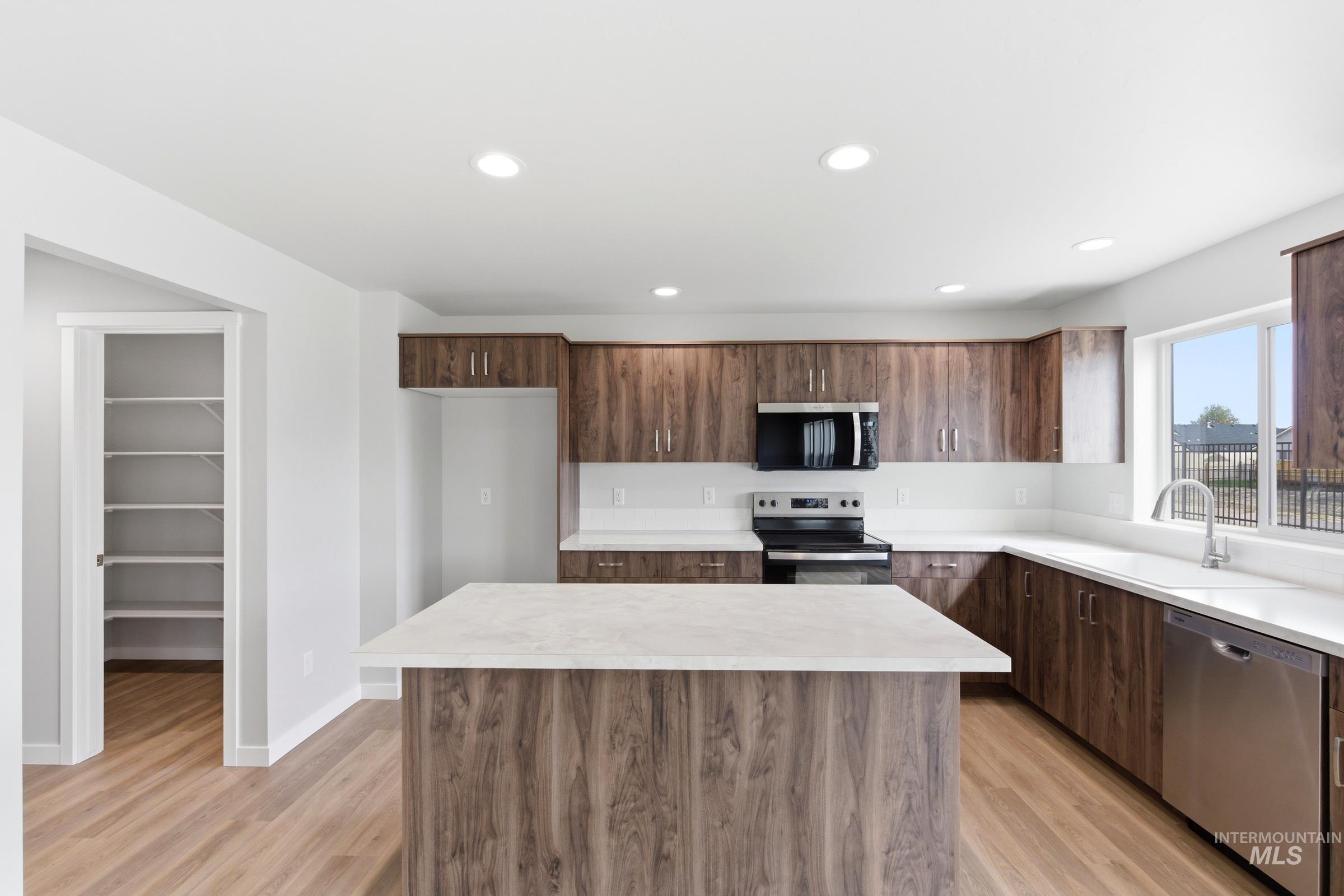 16558 Dunning Way Caldwell, ID 83607 - Photo 3 of 35 Kitchen featuring a central island with white countertop, wood-finish cabinetry, stainless steel appliances, and a dedicated pantry with extensive shelving