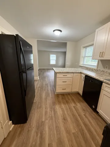 a kitchen with granite countertop a refrigerator a sink dishwasher and wooden cabinets with wooden floor