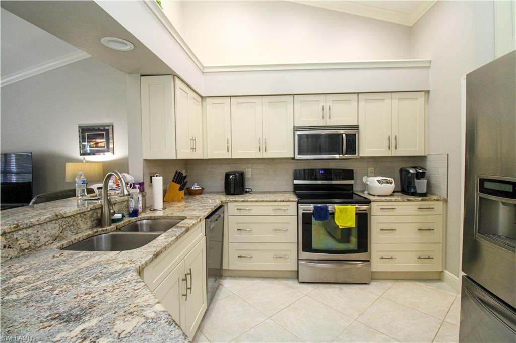 333 Wentworth Court Naples, FL 34104 - Photo 9 of 48 Kitchen with a sink, light stone counters, appliances with stainless steel finishes, crown molding, and light tile patterned floors