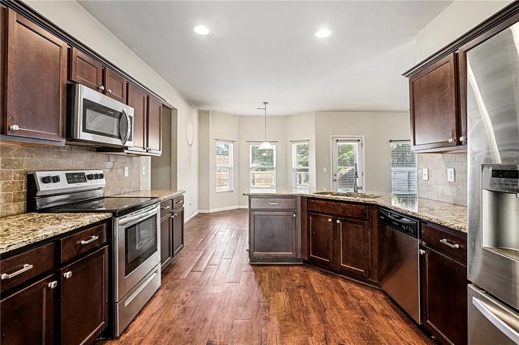 11046 Genova Terrace Hampton, GA 30228 - Photo 13 of 38 a large kitchen with stainless steel appliances granite countertop a stove top oven a sink dishwasher and wooden cabinets with wooden floor