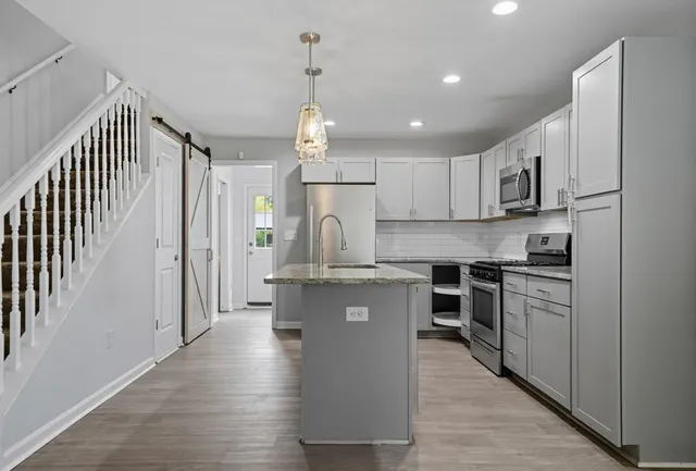 a kitchen with stainless steel appliances granite countertop a refrigerator a sink dishwasher a stove and white cabinets with wooden floor