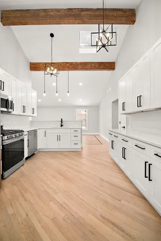 a large kitchen with stainless steel appliances a stove a sink and white cabinets with wooden floor