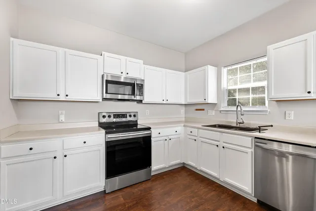 a kitchen with stainless steel appliances granite countertop a refrigerator a stove a sink and white cabinets with wooden floors