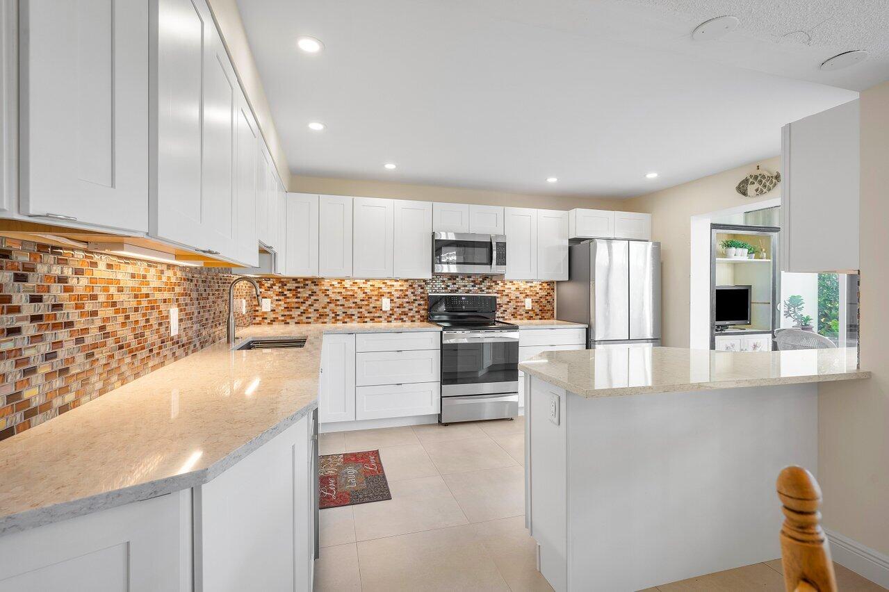 3677 Quail Ridge Drive, Unit BOBWHITE B Boynton Beach, FL 33436 - Photo 3 of 47 a kitchen with granite countertop a refrigerator oven a sink dishwasher and white cabinets next to a window