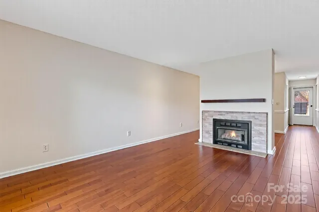 a view of an empty room with wooden floor fireplace and a window