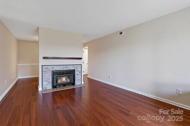 a view of an empty room with wooden floor fireplace and a window