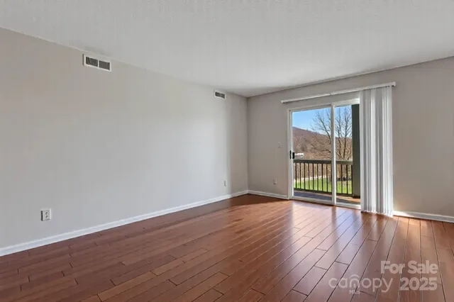 a view of an empty room with wooden floor and a window