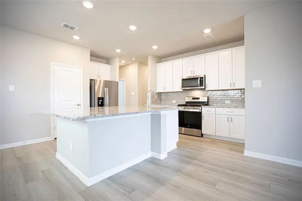 a kitchen with stainless steel appliances granite countertop a stove top oven a sink and white cabinets