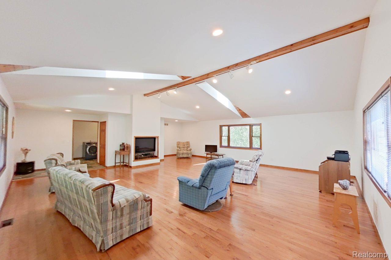 10201 Washburn Road Goodrich, MI 48438 - Photo 21 of 85 Spacious room featuring wood-finish flooring, vaulted ceilings with exposed beams, and a built-in fireplace with a hearth