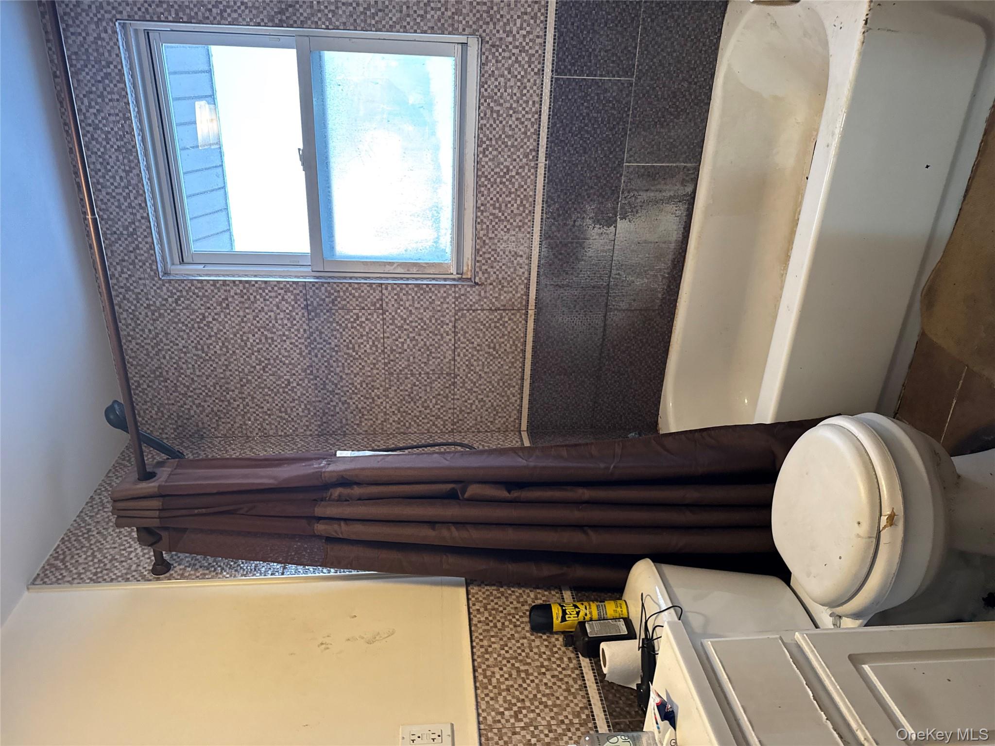 24-31 Deerfield Road Queens, NY 11691 - Photo 14 of 25 Bathroom featuring dark tile patterned flooring, shower / bath combo with shower curtain, vanity, wainscoting, and tile walls