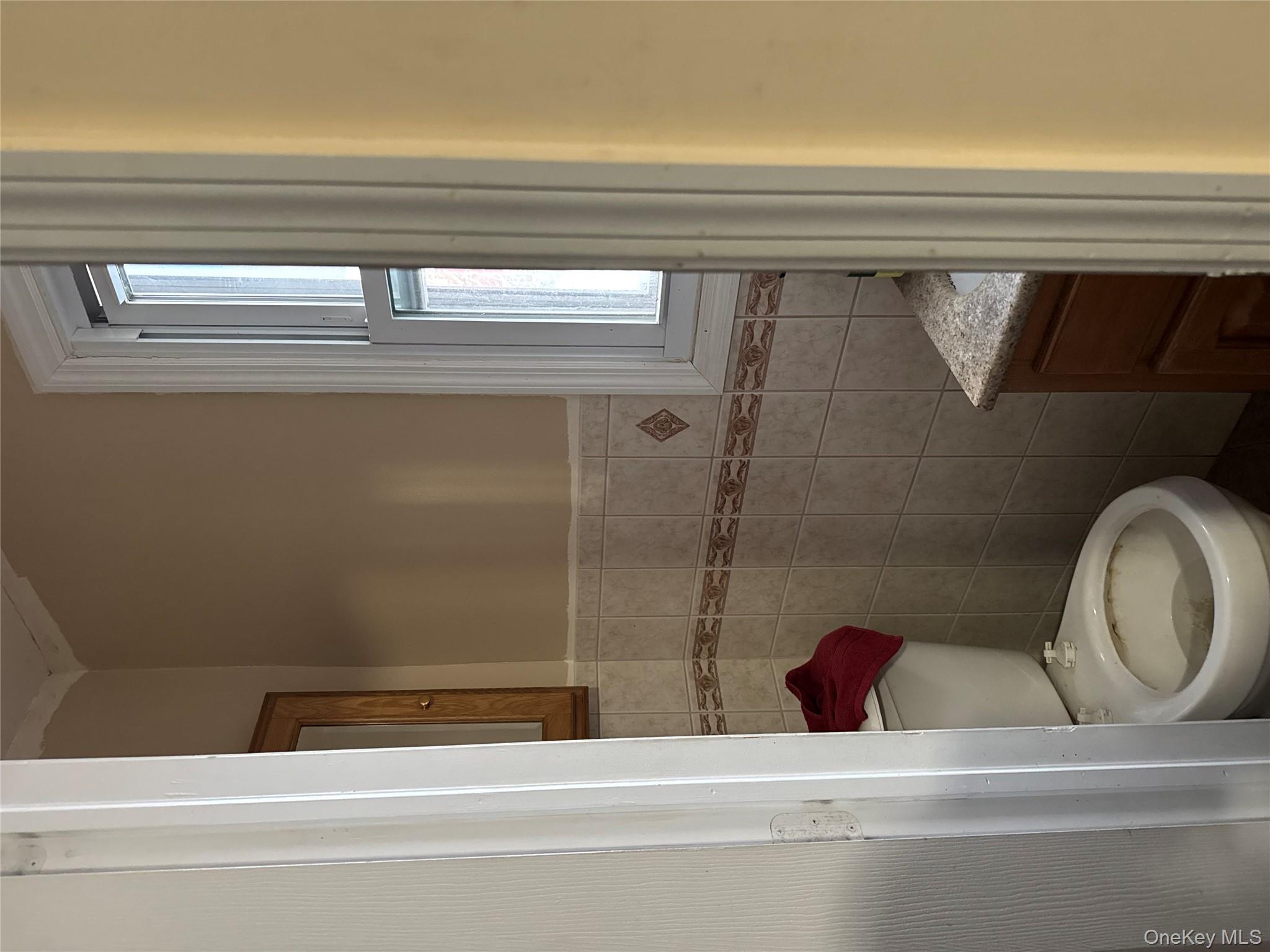 24-31 Deerfield Road Queens, NY 11691 - Photo 21 of 25 Half bath featuring vanity, tile walls, and wainscoting