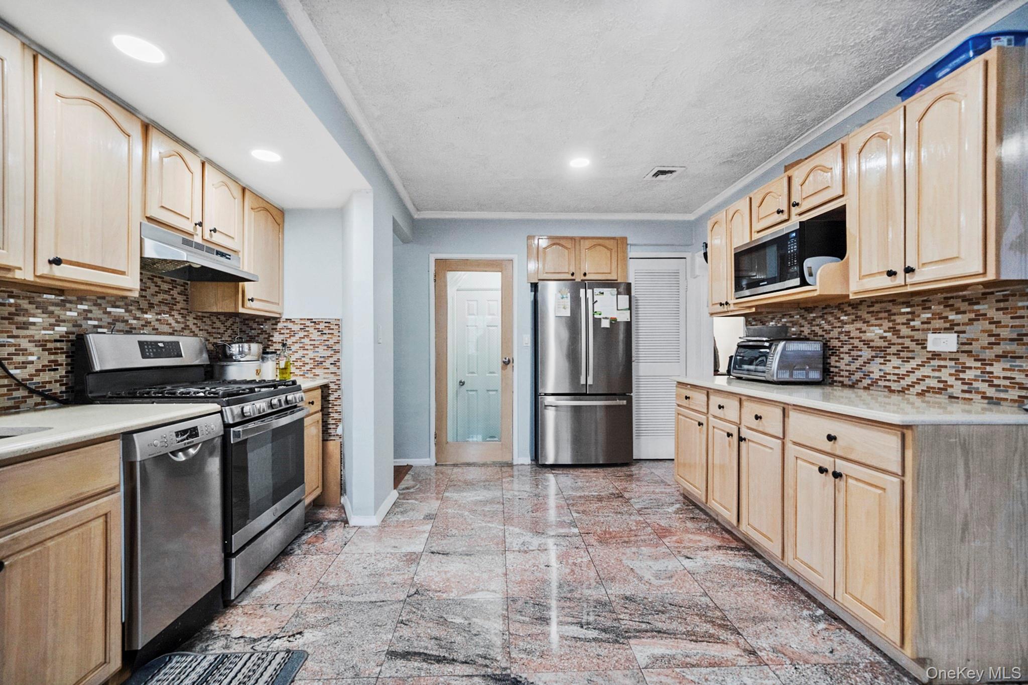 24-31 Deerfield Road Queens, NY 11691 - Photo 4 of 25 Kitchen featuring stainless steel appliances, tasteful backsplash, light brown cabinets, ornamental molding, and recessed lighting