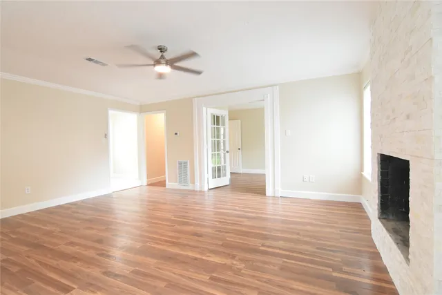 a view of an empty room with wooden floor and a ceiling fan