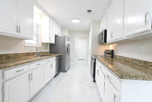 a kitchen with granite countertop a sink stainless steel appliances and white cabinets