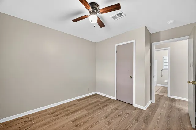 an empty room with wooden floor ceiling fan and windows